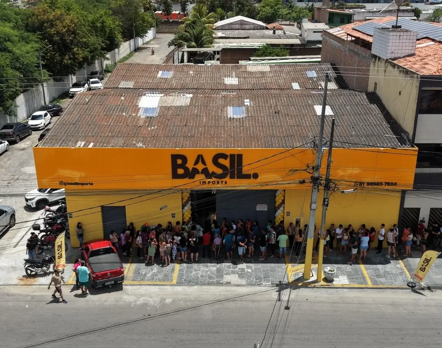 Vista aérea da fachada amarela da Basil Imports em Caruaru com fila de clientes na calçada durante a inauguração